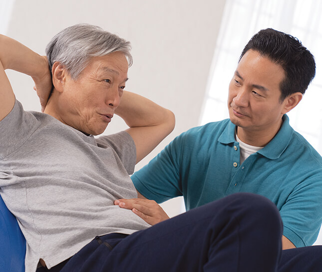 A physical therapist helping an older man with sit ups.